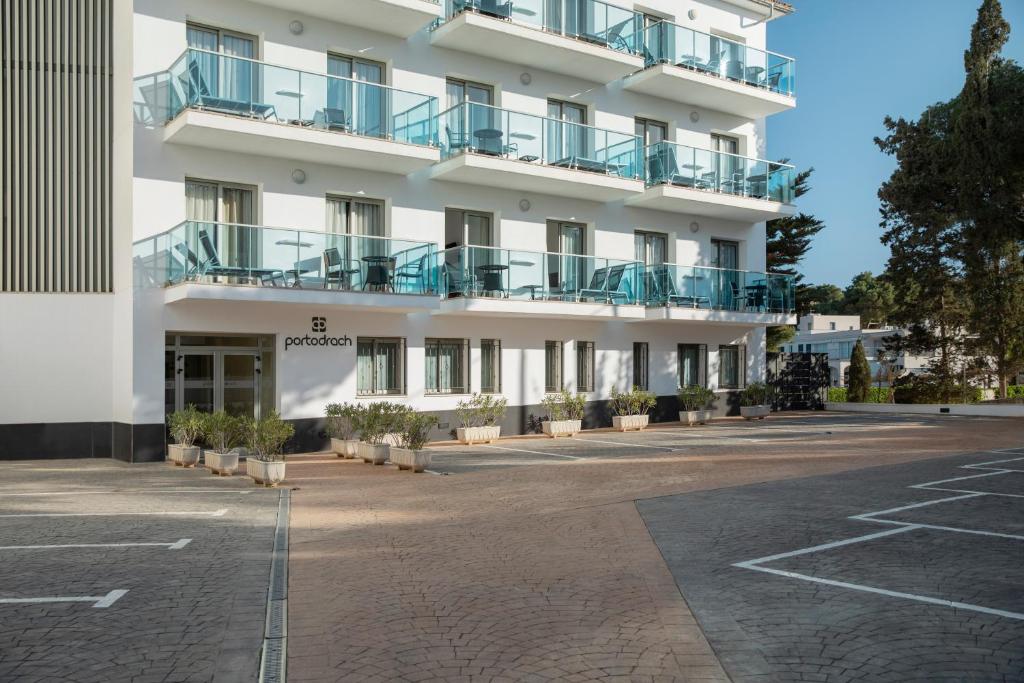 an empty parking lot in front of a white building at Porto Drach Aparthotel & Suites in Porto Cristo