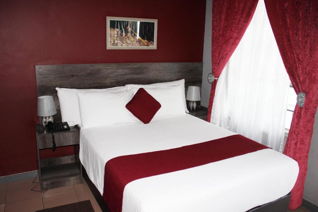 a bedroom with a large white bed with red curtains at Platinum Hotel in Gaborone