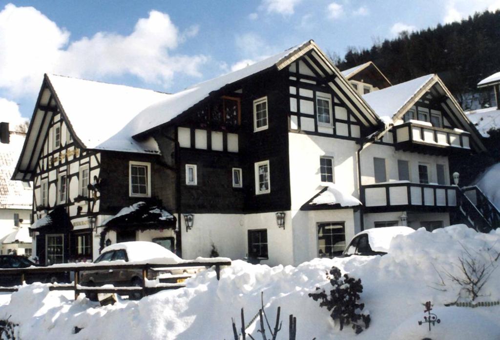 uma casa grande coberta de neve com carros na frente em Hotel-Restaurant Zum Dorfkrug em Winterberg