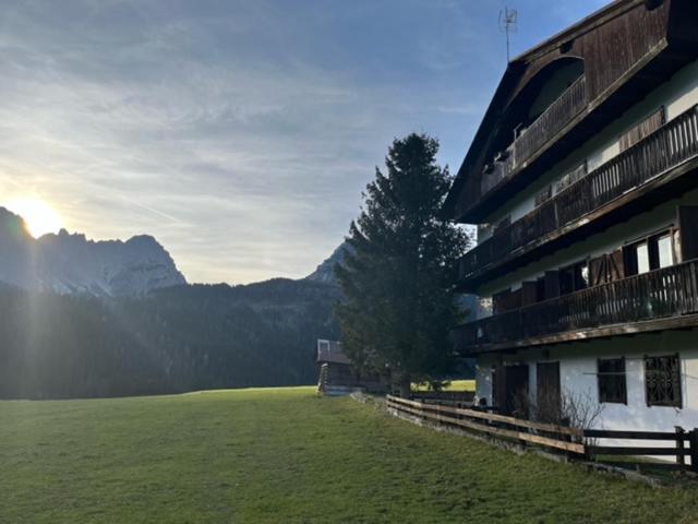a building with a green field next to a mountain at Condominio Dorf in Sappada