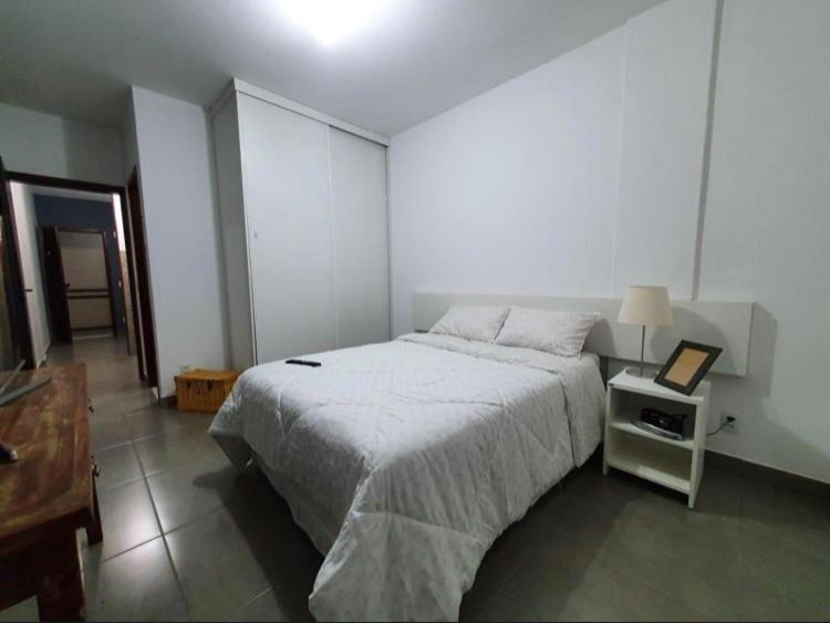 a white bedroom with a bed and a night stand at Apartamento aconchegante no Sudoeste in Brasília