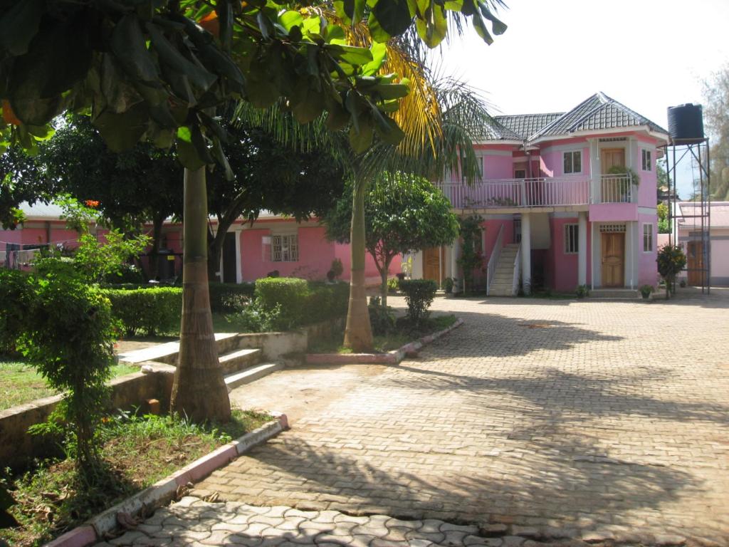 ein rosafarbenes Haus mit Bäumen davor in der Unterkunft R&R Gardens Hotel in Mbale