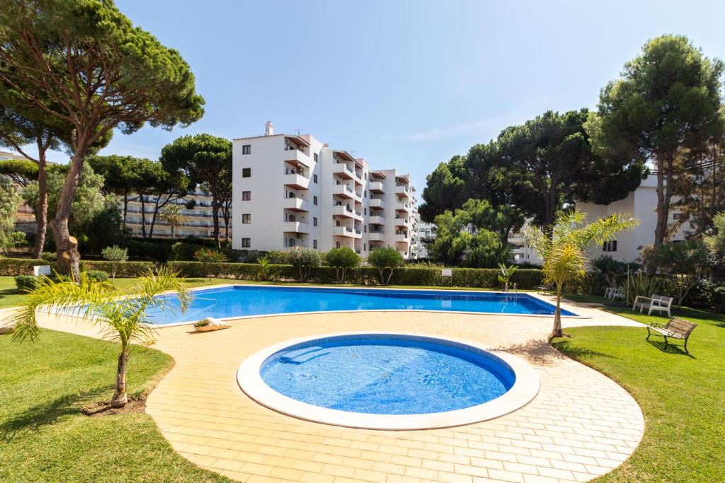 a swimming pool in a garden with a building in the background at Great, Bright 2-bedroom Flat in the Center of Vilamoura -Topázio By Centralgarve in Vilamoura