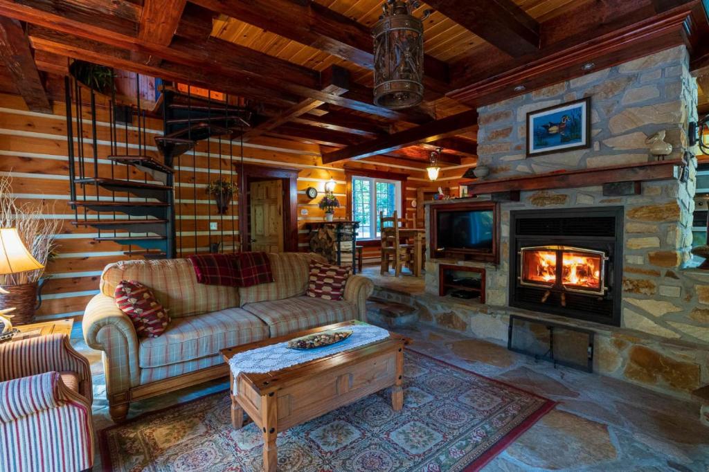 a living room with a stone fireplace in a log cabin at Domaine Rivière Sacacomie in Saint-Alexis-des-Monts