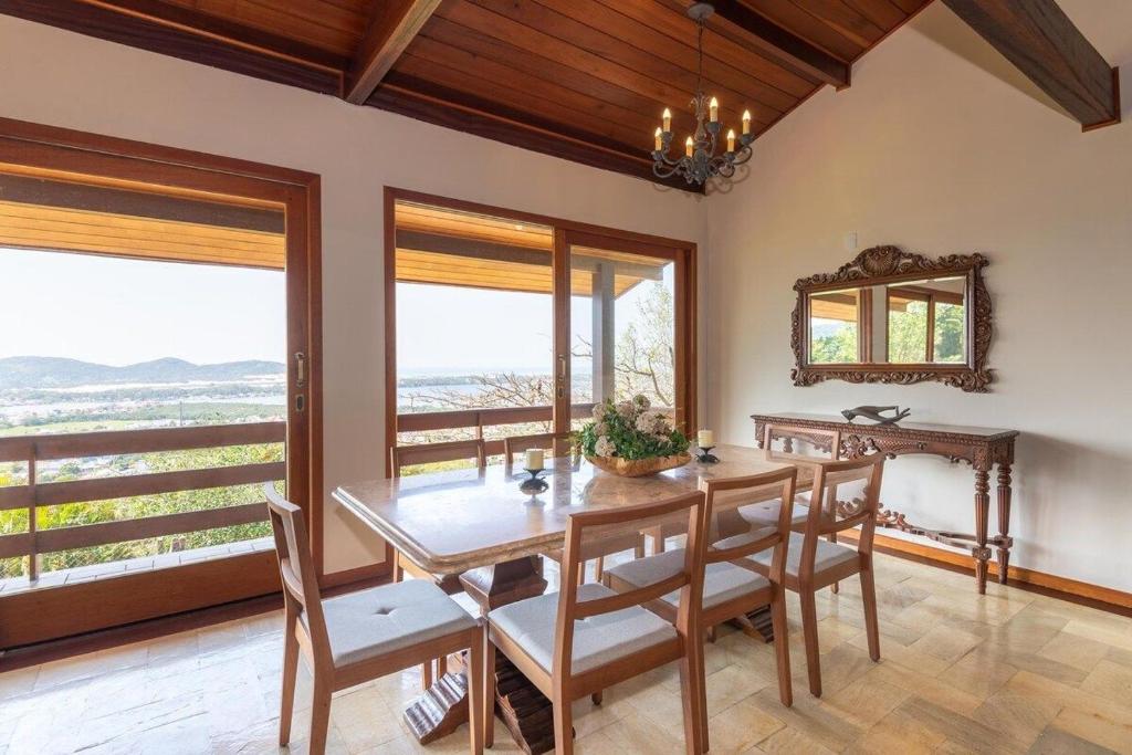 a dining room with a table and chairs and windows at Mansão Linda Vista Lagoa da Conceição Jacuzzi in Florianópolis