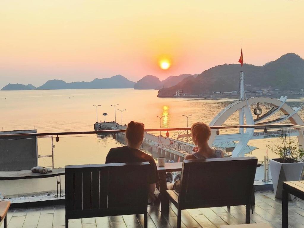 un hombre y una mujer sentados en una mesa viendo la puesta de sol en Catba Pod Hostel en Cat Ba