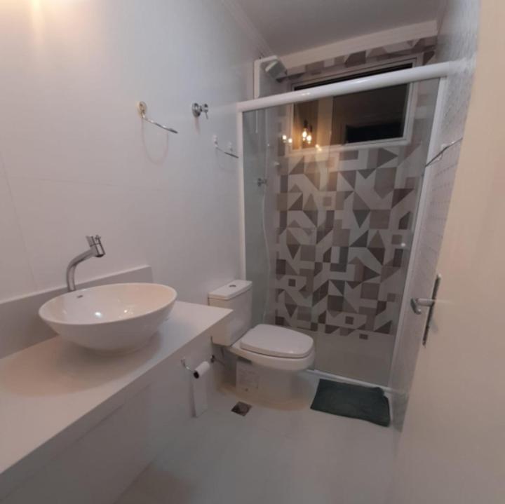 a white bathroom with a toilet and a sink at Apartamento pé na areia in Guarujá
