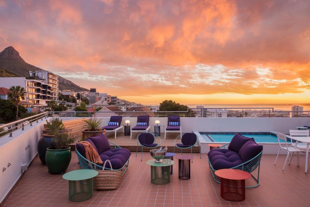 una terraza en la azotea con sillas, mesas y una puesta de sol en Home Suite Hotels Sea Point, en Ciudad del Cabo