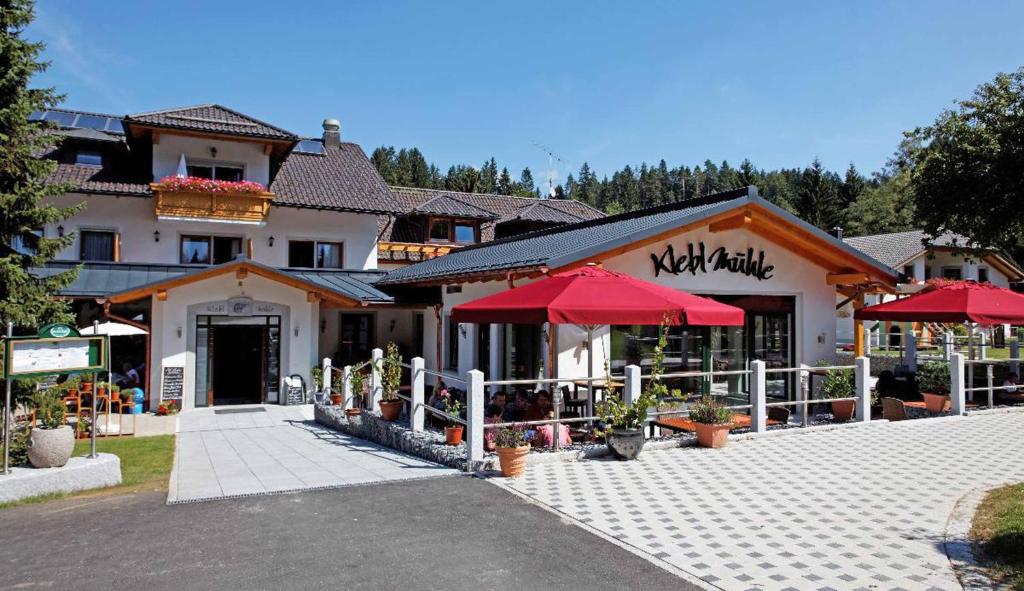 un restaurante con sombrillas rojas frente a un edificio en Landhotel Kleblmühle en Grafenau