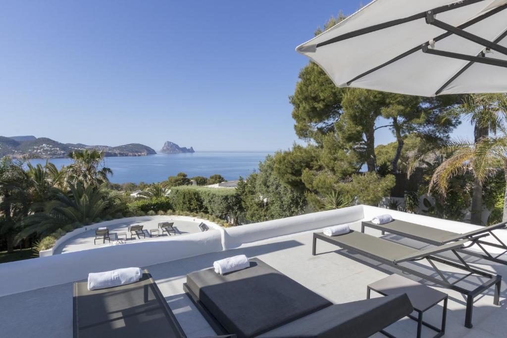 a patio with chairs and an umbrella and the ocean at Magical Ibizan Villa Walking Distance To The Beach Es Vedra Style 6 Bedrooms Fabulous Sea Views San Jose in Sant Josep de Sa Talaia