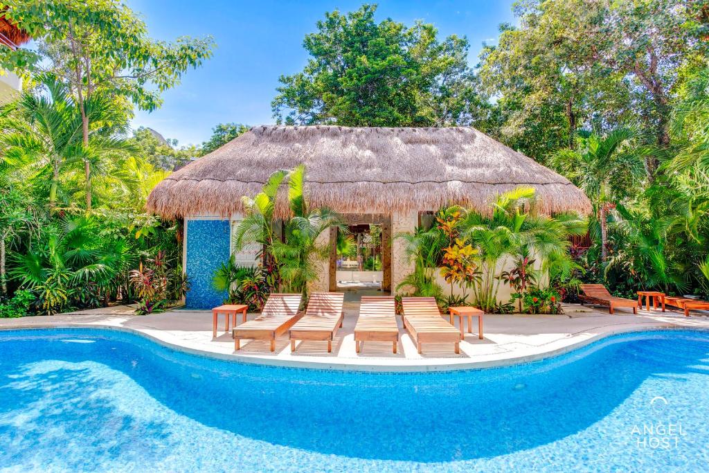 um resort com piscina e cadeiras e um edifício com telhado de palha em Condo Complex with an Alluring Pool & Tropical Vibes by Stella Rentals em Tulum