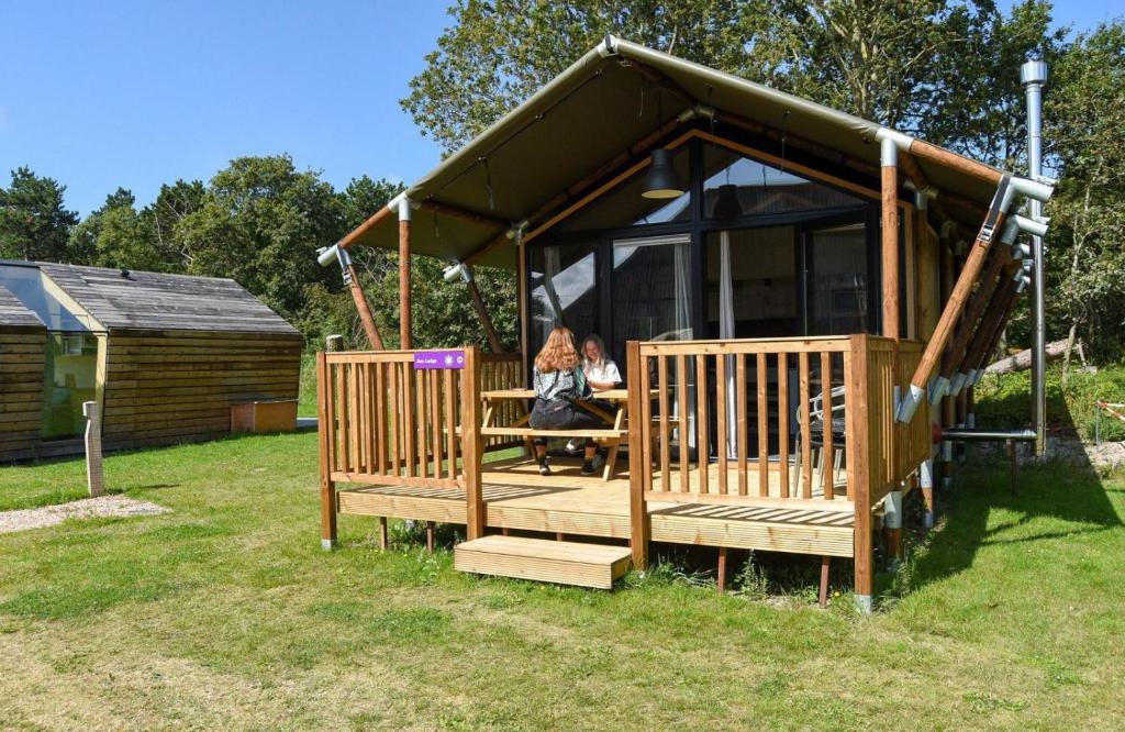 a woman sitting at a table in a gazebo at Safari Lodge, glamping aan zee! in Callantsoog