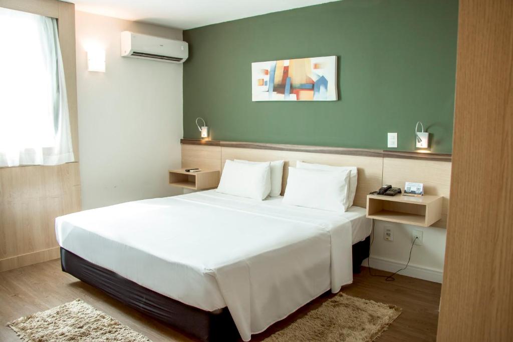 um quarto com uma cama branca e uma parede verde em Comfort Hotel Campos dos Goytacazes em Campos dos Goytacazes