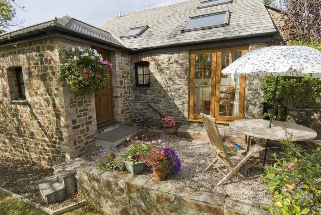 a stone house with a table and an umbrella at Shipload Cottage in Hartland