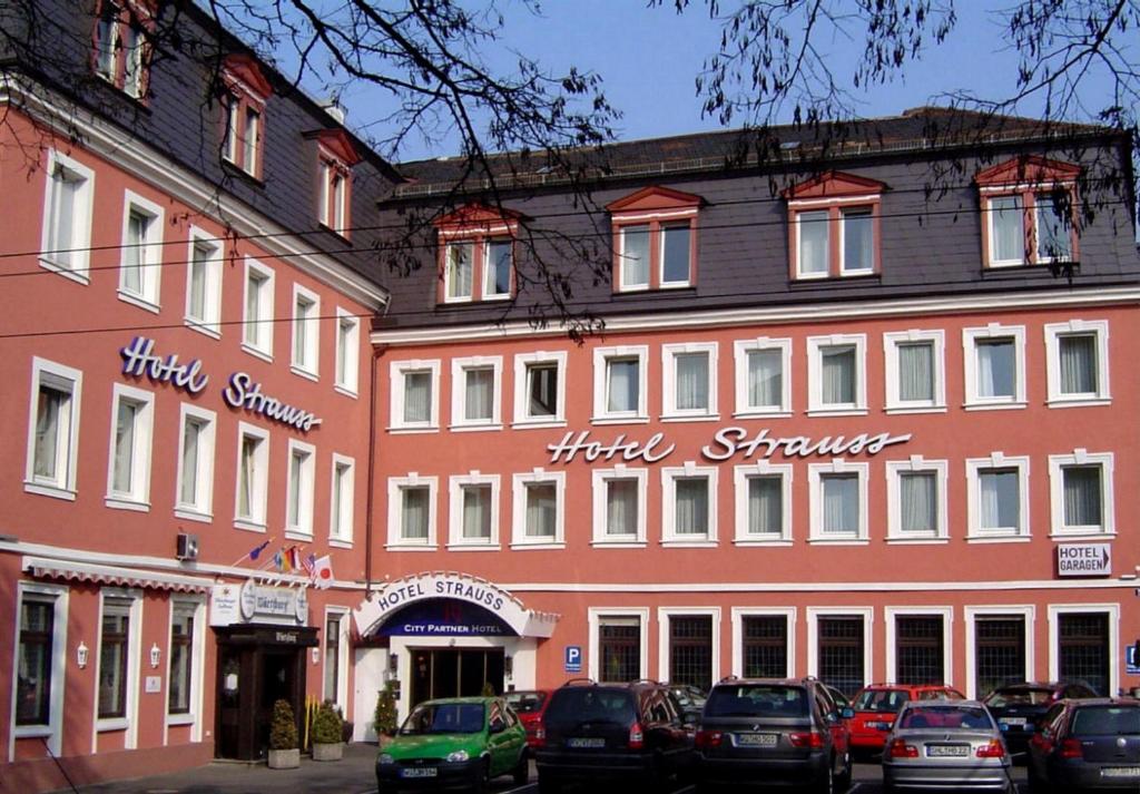 un grand bâtiment rouge avec des voitures garées devant lui dans l'établissement City Partner Hotel Strauss, à Wurtzbourg