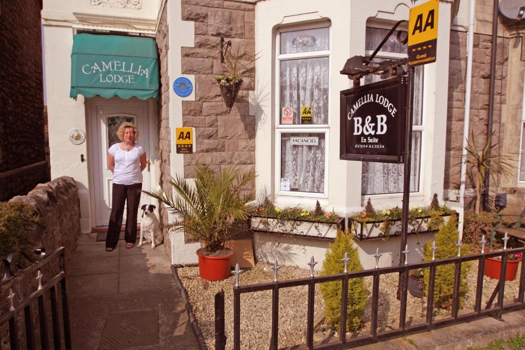 Una donna in piedi sulla porta di un palazzo con un cane di Camellia Lodge Guest House a Weston-super-Mare