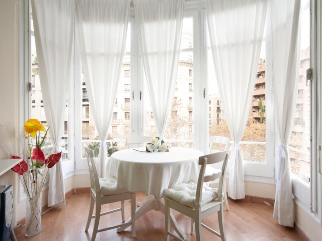 uma sala de jantar branca com uma mesa, cadeiras e janelas em Hostal Felipe 2 em Barcelona