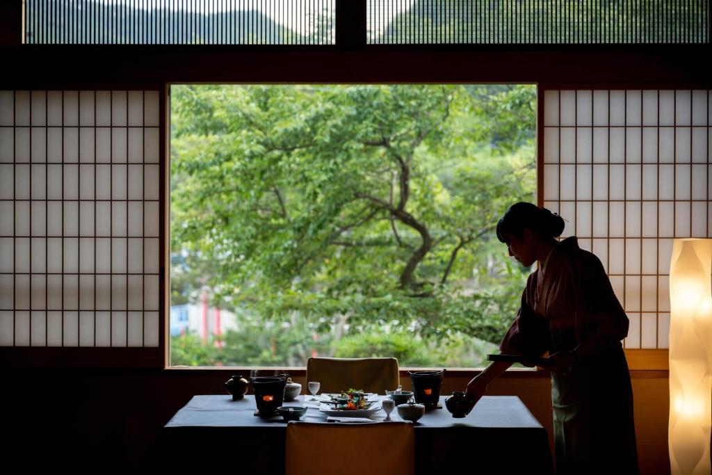 eine Person, die vor einem Tisch mit einem Fenster steht in der Unterkunft Eirakukan in Koriyama