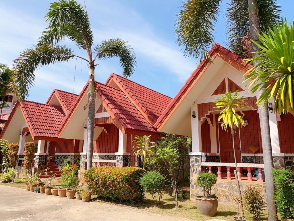 een huis met een rood dak en palmbomen bij Bunraksa Resort in Kamphaeng Phet