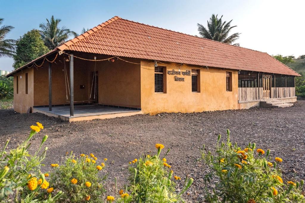 a small building with a porch in a field of flowers at CosmicStays Rustic Elegance - Traditional Wada Inspired Living in Shirwal