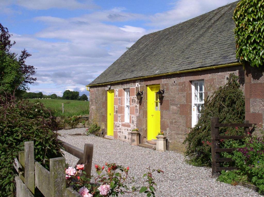 un pequeño edificio de piedra con puerta amarilla en Ballat Smithy Cottage, en Drymen