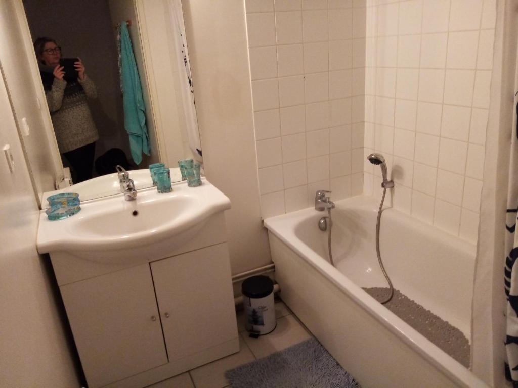 una donna che scatta una foto di un bagno con lavandino e vasca di Chez Maniche a Cayeux-sur-Mer