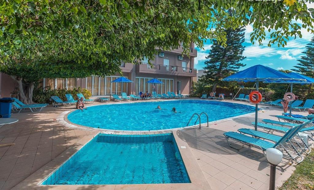 a swimming pool with blue chairs and people in it at Castro Hotel in Amoudara Herakliou