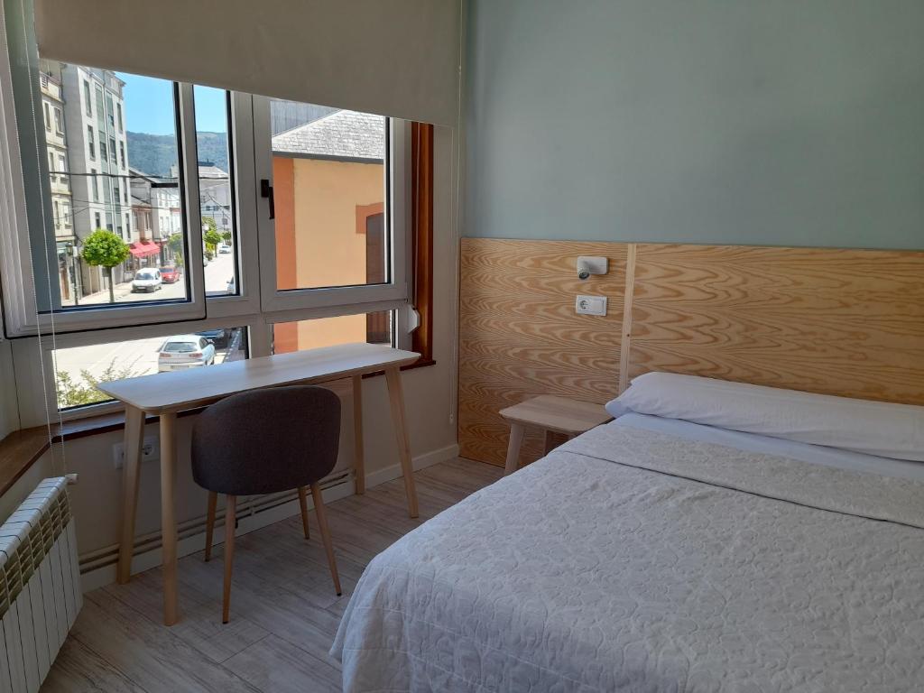 a bedroom with a bed and a desk and a window at Hostal Quiper in Quiroga
