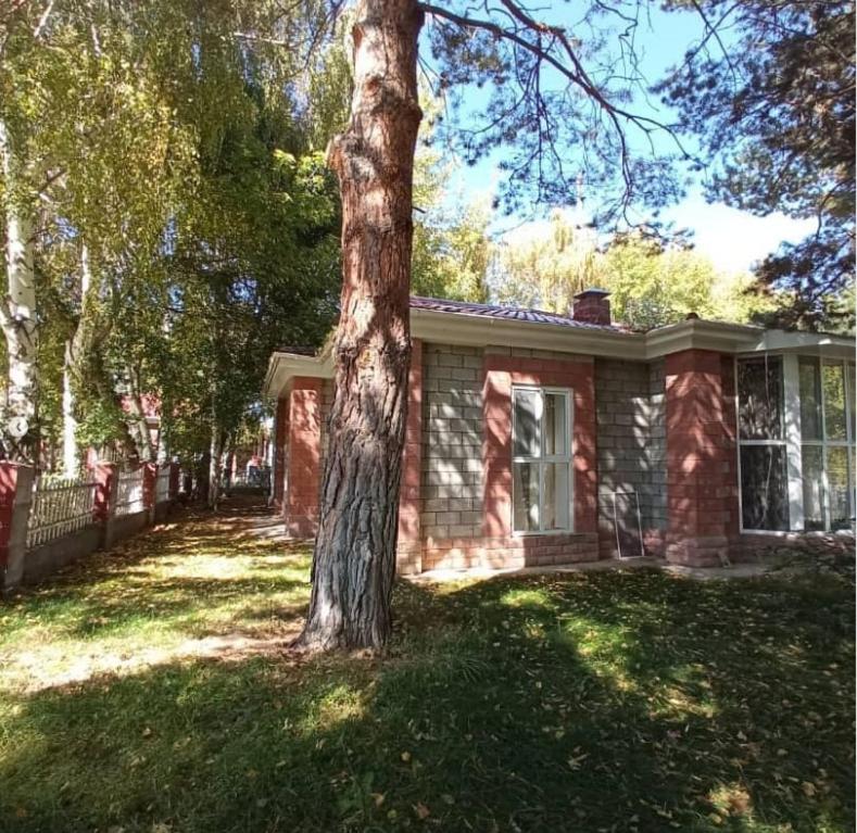 una casa de ladrillo con un árbol en el patio en Raduga West Pineforest - коттедж в аренду на Иссык-Куле en Koshkolʼ