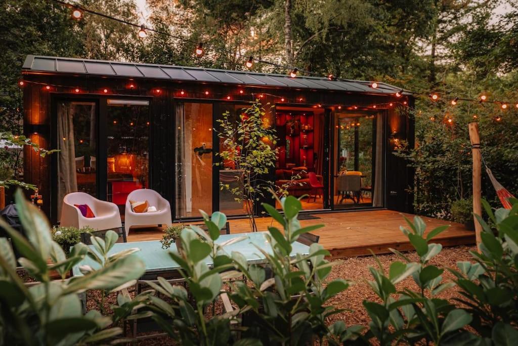 een tiny house met een terras, stoelen en verlichting bij Coco’s Buitenhuisje in Nunspeet