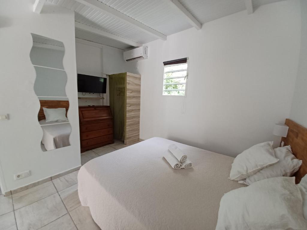 a white bedroom with a bed and a television at La Rose du Bresil Marie-Galante in Capesterre