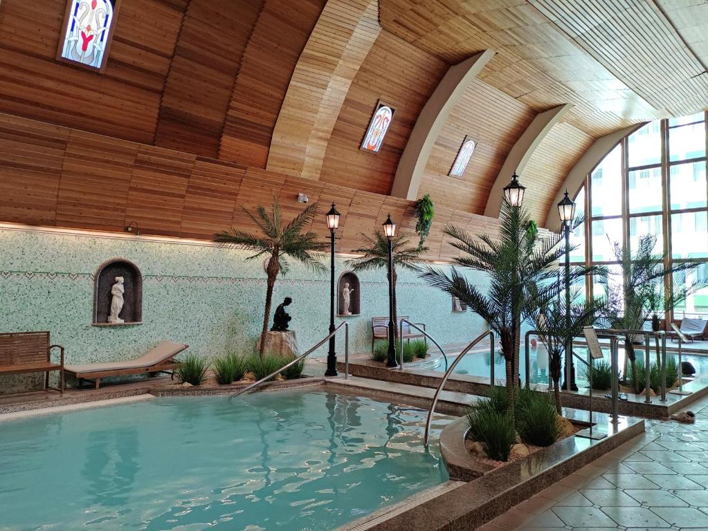 a large indoor pool in a building with palm trees at Spa Residence Carbona Mona Lila Apartman in Hévíz