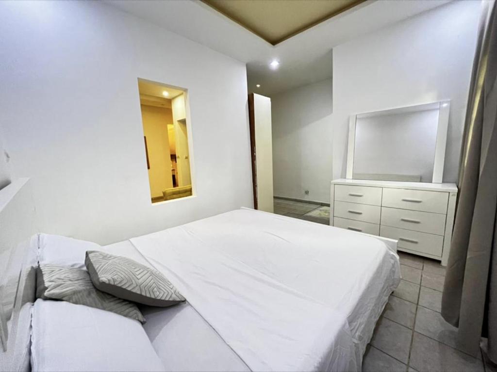 Dormitorio blanco con cama blanca y espejo en Appartement Cosy au Centre des Mamelles By Hestia Lights, en Dakar