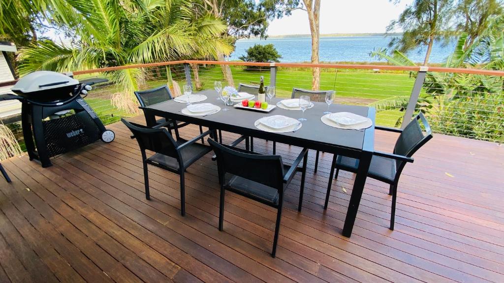 une table et des chaises noires sur une terrasse avec un grill dans l'établissement Absolute lakefront house - enjoy the sunrise, à Budgewoi