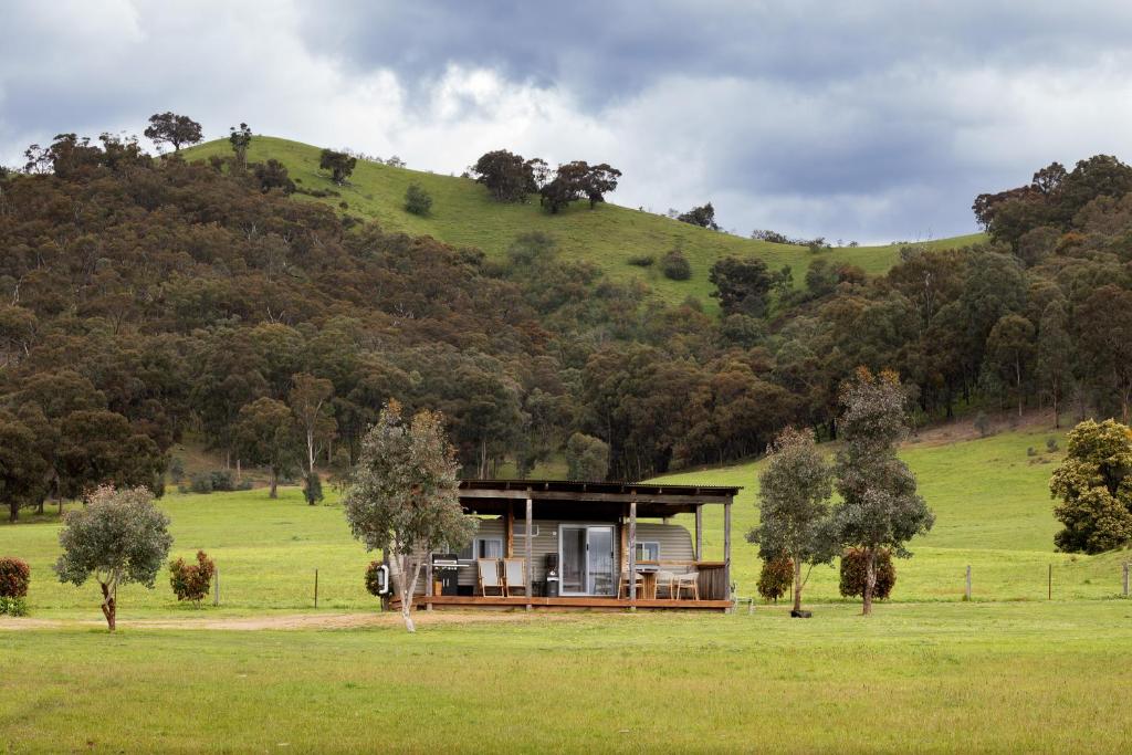 a house in a field with a hill in the background at The Village Green Glampervans in Strath Creek
