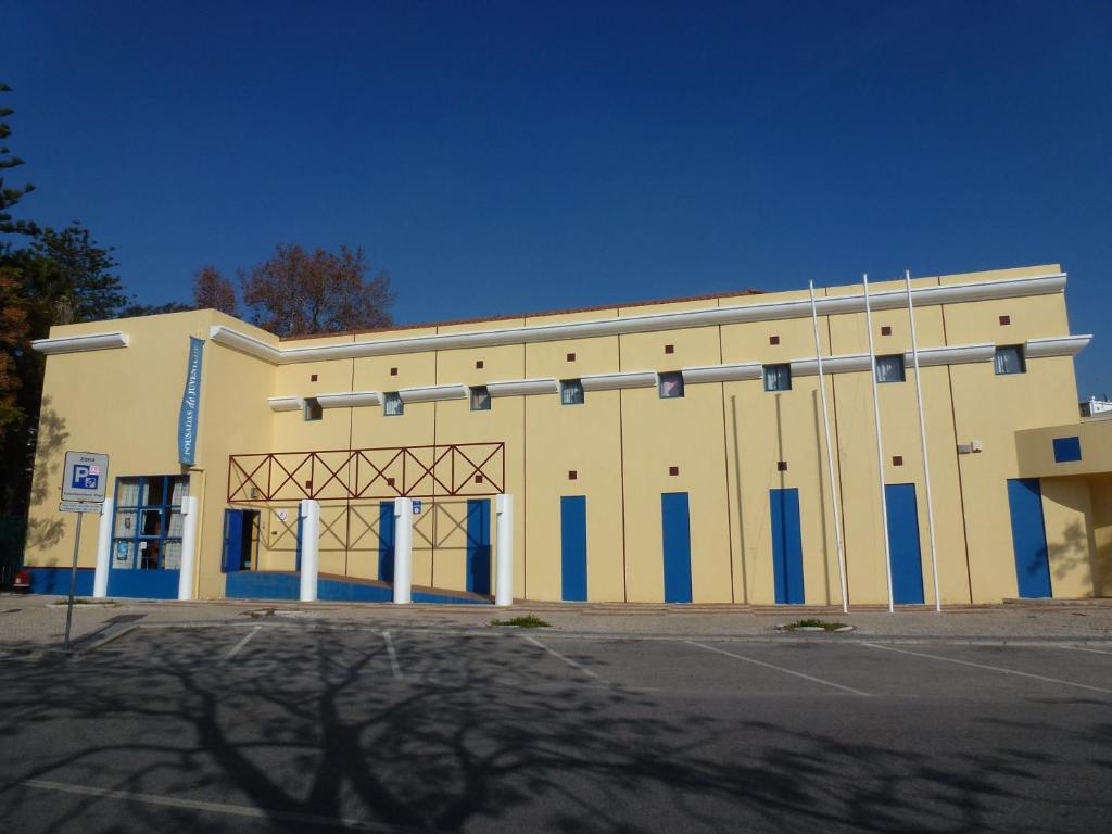 duży żółty budynek z niebieskimi drzwiami i parkingiem w obiekcie HI Faro – Pousada de Juventude w Faro