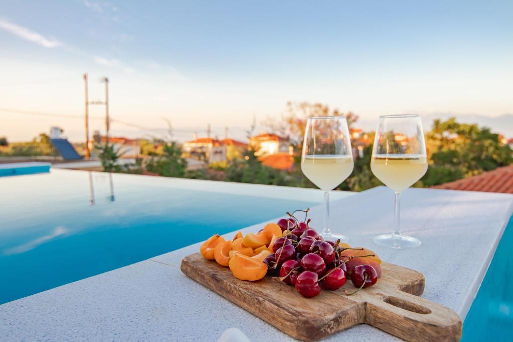 a plate of fruit and two glasses of wine on a table at Georgianna's suite with private pool , 'blank suite' in Kharokopión