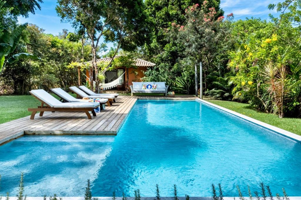 a swimming pool with a wooden deck and chairs next to it at Casa Laranjeiras, Rio da Barra beach, Trancoso in Trancoso