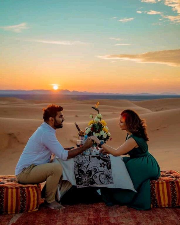 sahara luxury desert camp في أرفود: يجلس رجل وامرأة على طاولة في الصحراء