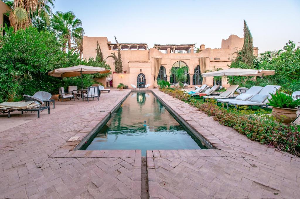 a pool in a courtyard with chairs and umbrellas at Prestige du Souss in Oulad Berhil
