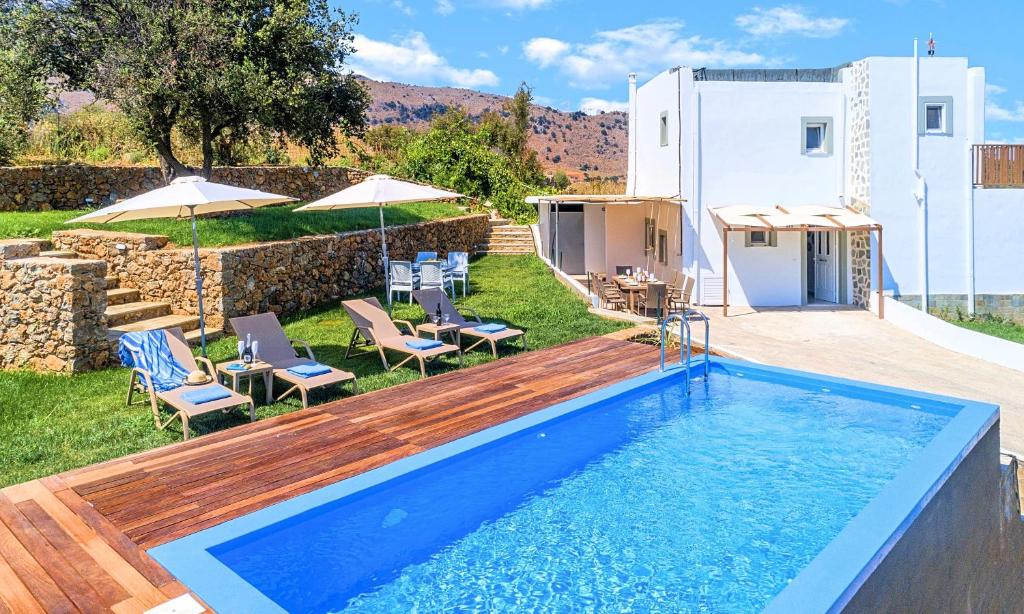 una piscina en un patio trasero con sillas y sombrillas en Georgioupolis Blue Villa, en Georgioupolis