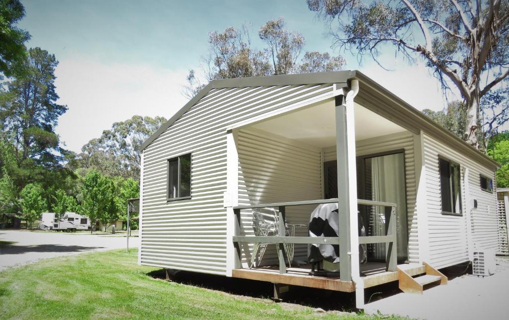 a small white tiny house with a porch at Beechworth Holiday Park in Beechworth
