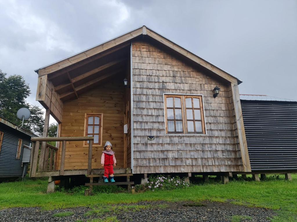 a little girl standing on the porch of a tiny house at Cabañas Quilquico in Quilquico