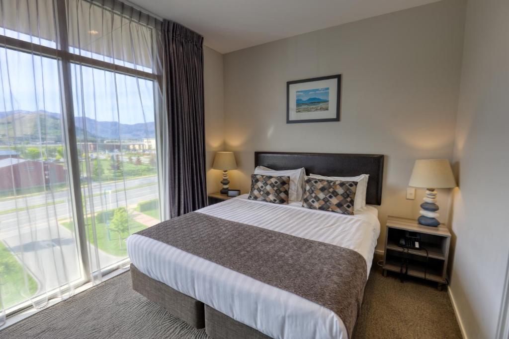 a bedroom with a large bed and a large window at Ramada Suites by Wyndham Queenstown Remarkables Park in Queenstown