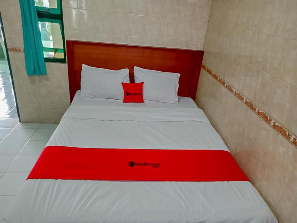 a bed with a red pillow on top of it at RedDoorz Syariah @ Hotel Sidomulyo Pacitan in Pacitan