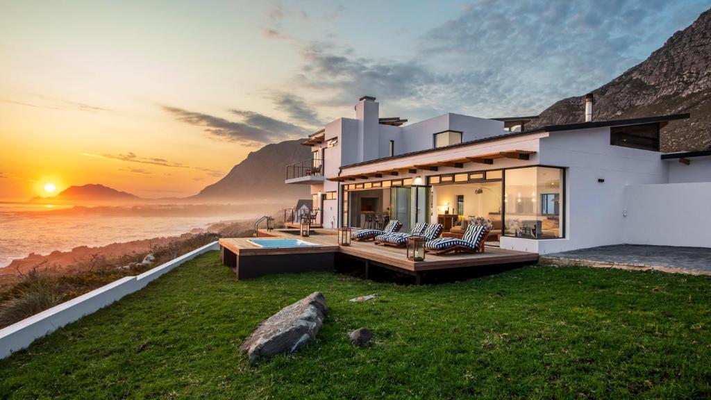a house with a view of the ocean at sunset at OnTheRocksBB Solar Powered Guesthouse and Ocean Lodge in Bettyʼs Bay
