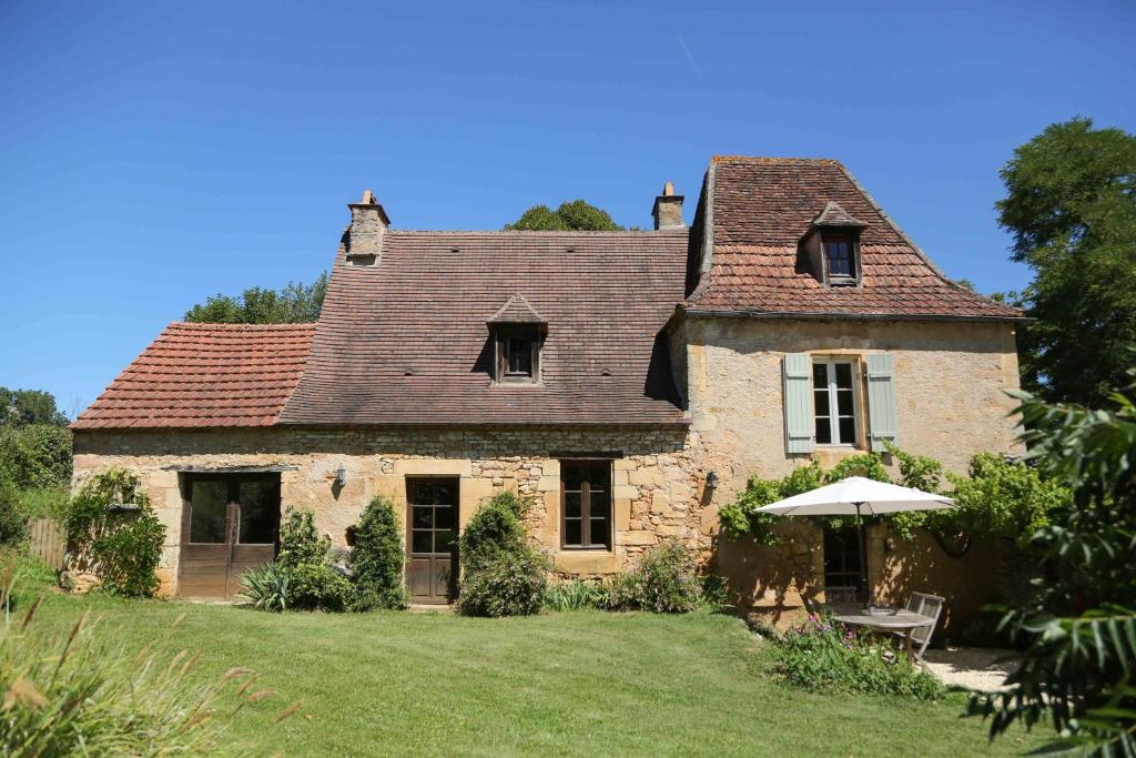 an old stone house with an umbrella in the yard at La Maison de Jardin à La Peyrière in Le Bugue