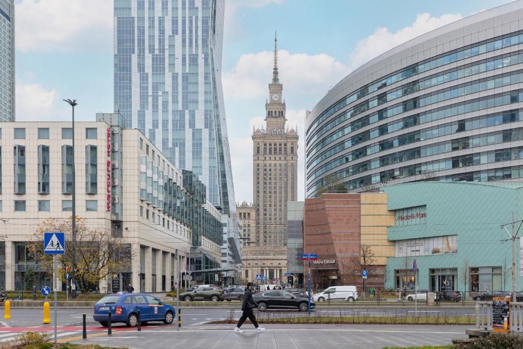 a person crossing a street in a city with a clock tower at Złota Apartment Center of Warsaw by Renters in Warsaw