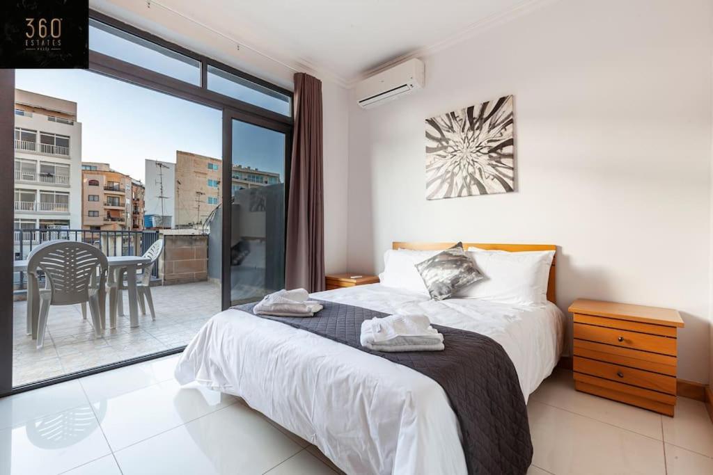 1 Schlafzimmer mit einem Bett und einem Balkon mit einem Tisch in der Unterkunft Comfortable Penthouse, served with LIFT, WIFI & AC by 360 Estates in Gżira