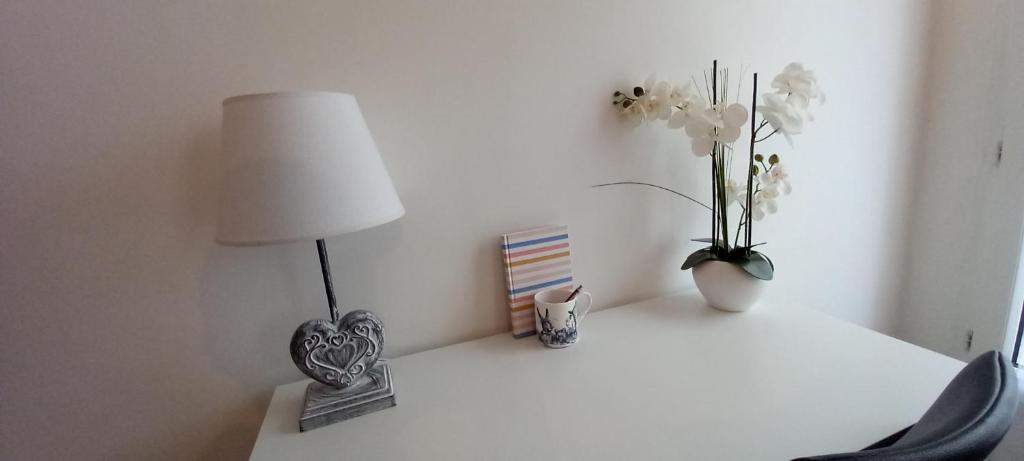 einem weißen Tisch mit einer Lampe und Blumen darauf in der Unterkunft Studio Meublé in Bussy-Saint-Georges